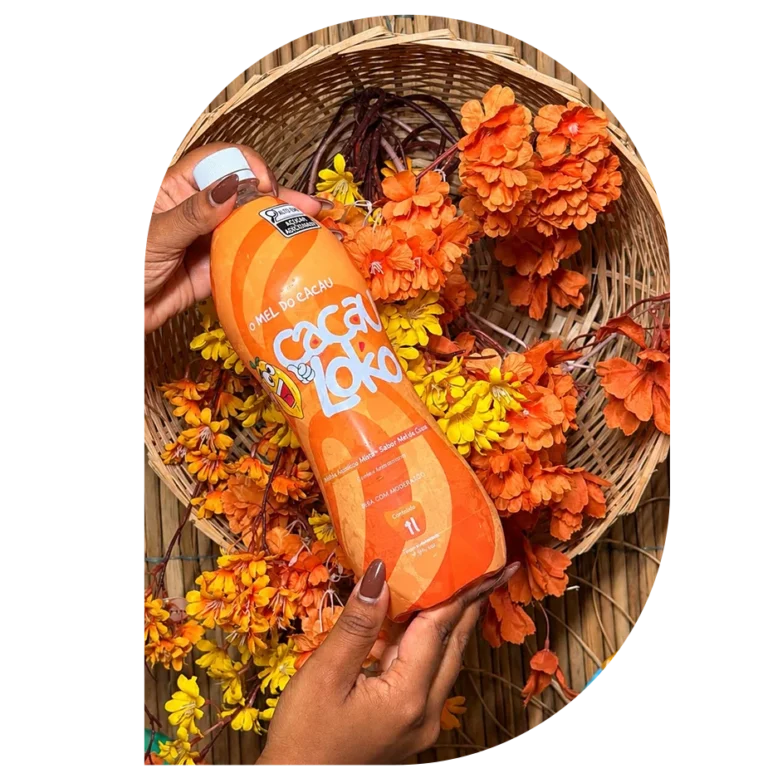 Mão segurando a garrafa de Cacau Loko sobre um cesto com flores laranja